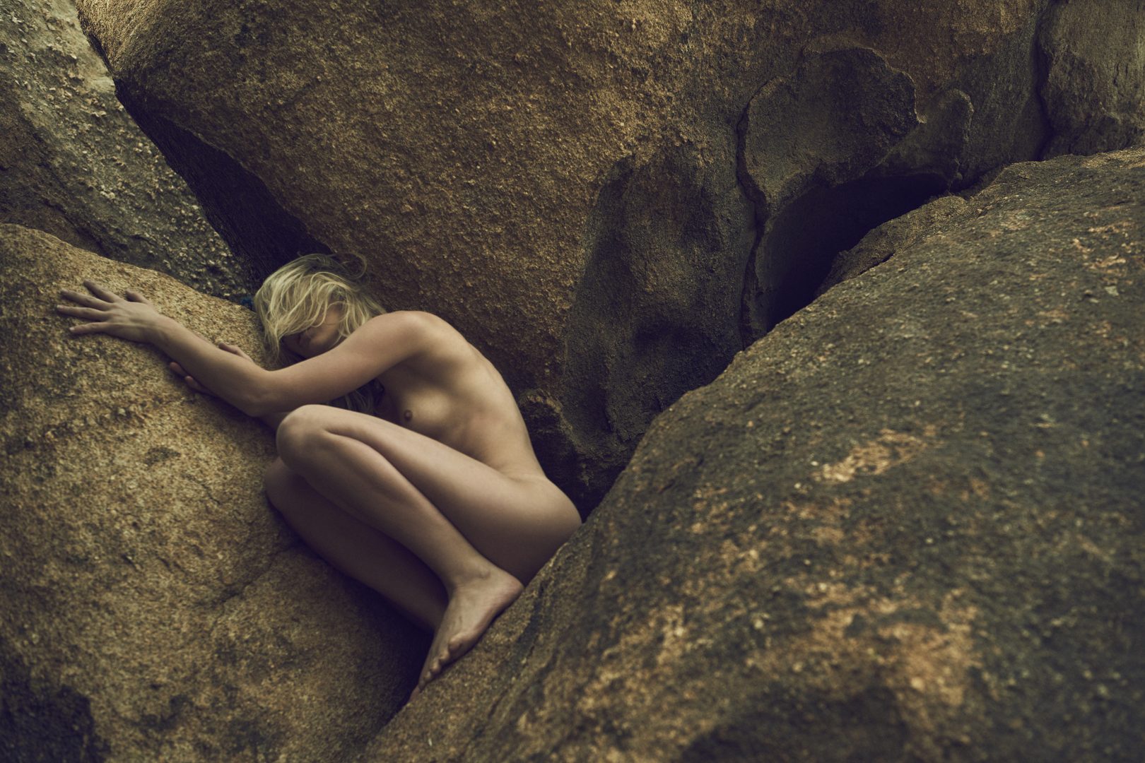 Naked girl climbing up rock in the desert by Stefan Rappo