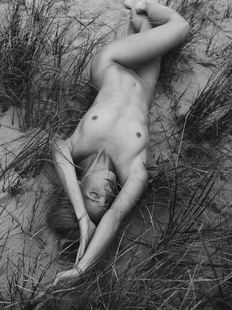 Naked girl lying on the beach between grass by Stefan Rappo