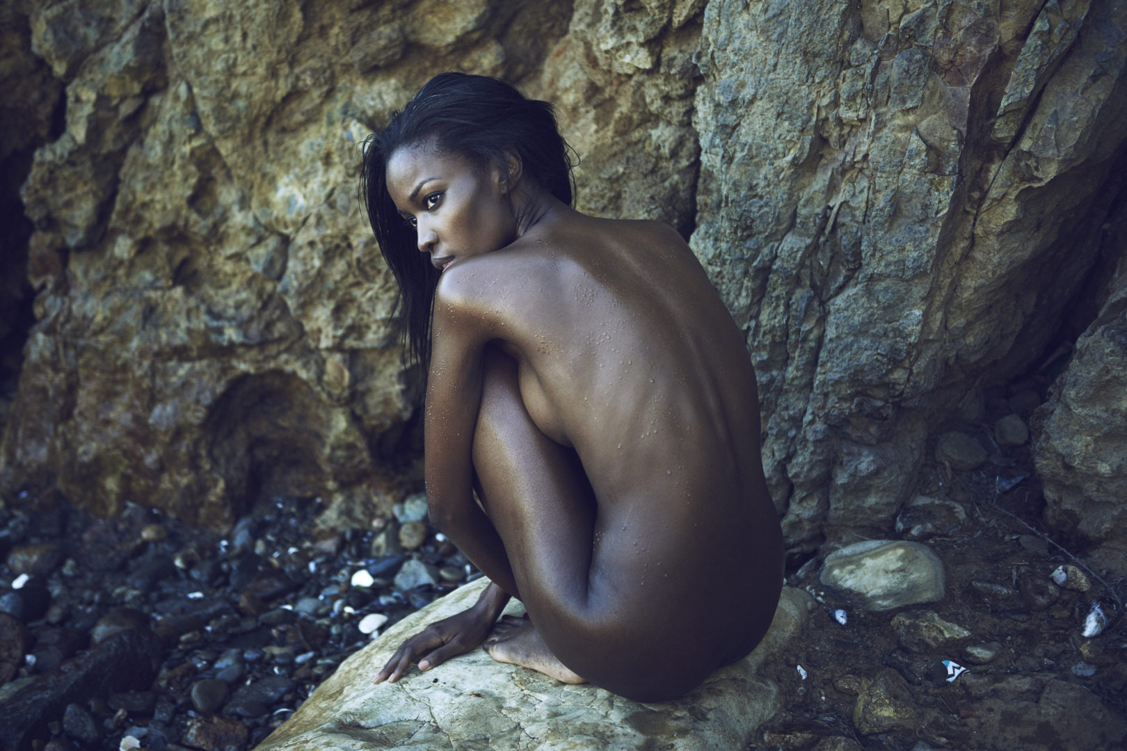 Naked girl on beach in front of big rock by Stefan Rappo