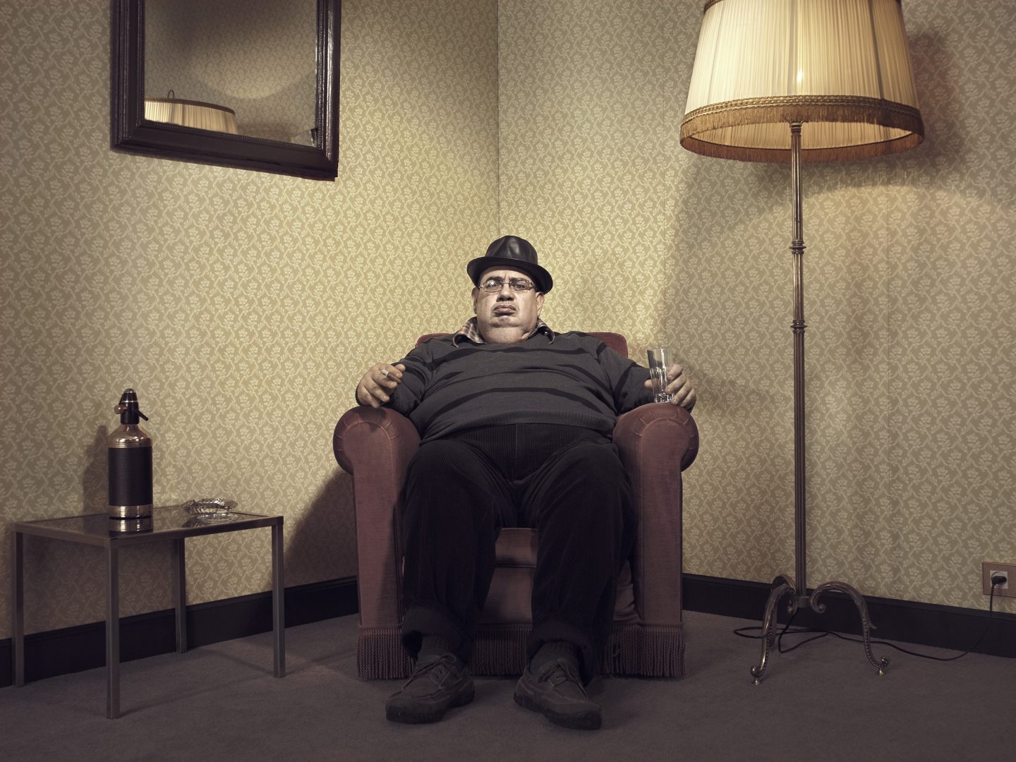 Man with hat sitting in armchair in room 42 by Stefan Rappo