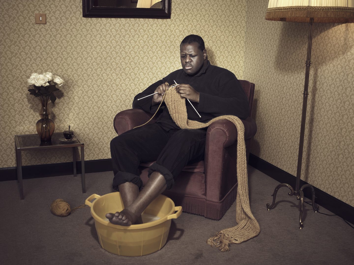 Black man sitting in armchair and knitting in room 42 by Stefan Rappo