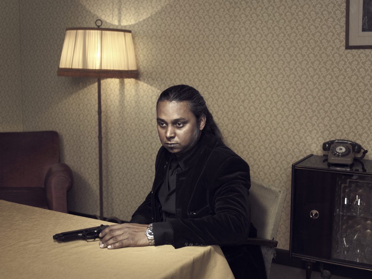 Man with gun sitting at table in room 42 by Stefan Rappo
