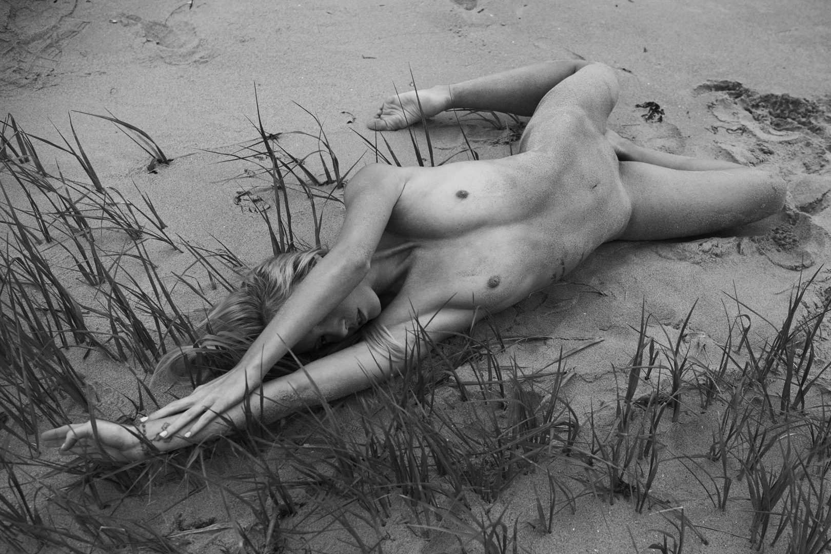 Naked girl lying on the beach between grass by Stefan Rappo